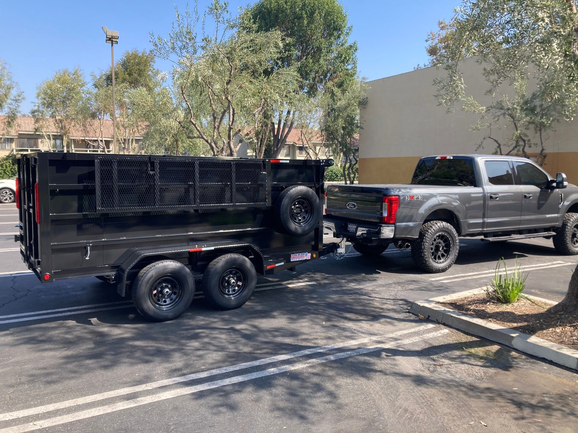 Gray heavy-duty pickup truck hitched to a black dump trailer in a community parking lot